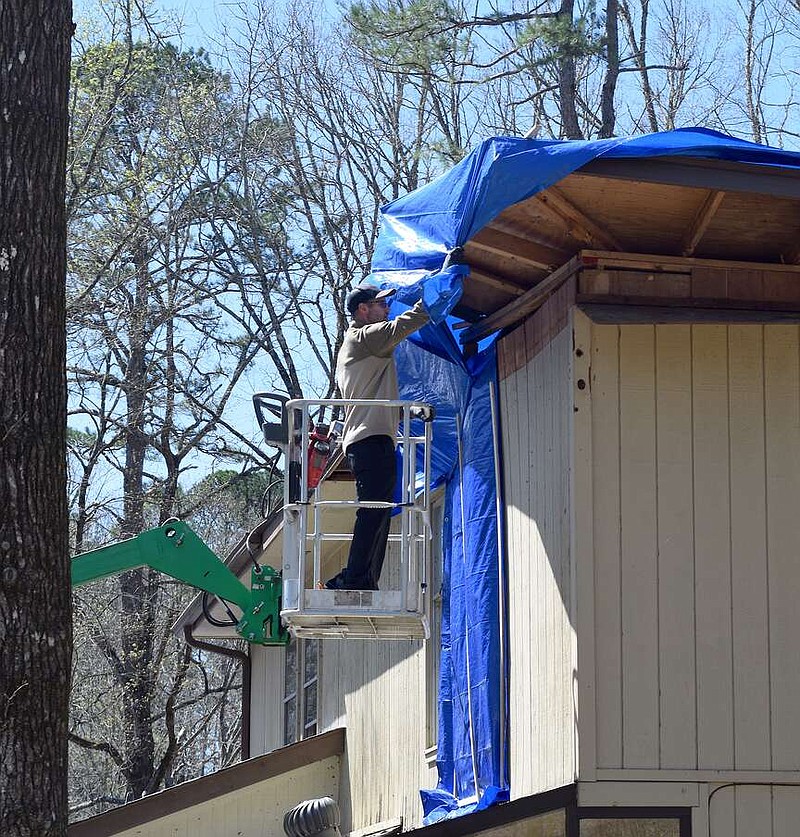 A man on a lift works to put a tarp on a roof that was damaged by the March 14 tornado in Hot Springs Village. (The Sentinel-Record/Donald Cross)