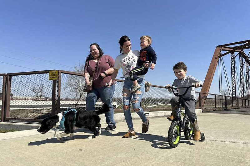 Emerson Howard and dog Dixie, from left, enjoy a walk along with Destiny Porter and her children, 2-year old Merrick Mercer and 4-year old Maxton Mercer, at the Kitselman bridge connecting the Cardinal and White River Greenway trails on Wednesday, March 13, 2024, in Muncie, Ind. The Cardinal Greenways pathway born from eastern Indiana's abandoned railroad tracks will become a central cog in the Great American Rail Trail — a planned 3,700-mile network of uninterrupted trails spanning from Washington state to Washington, D.C. (AP Photo/Isabella Volmert)