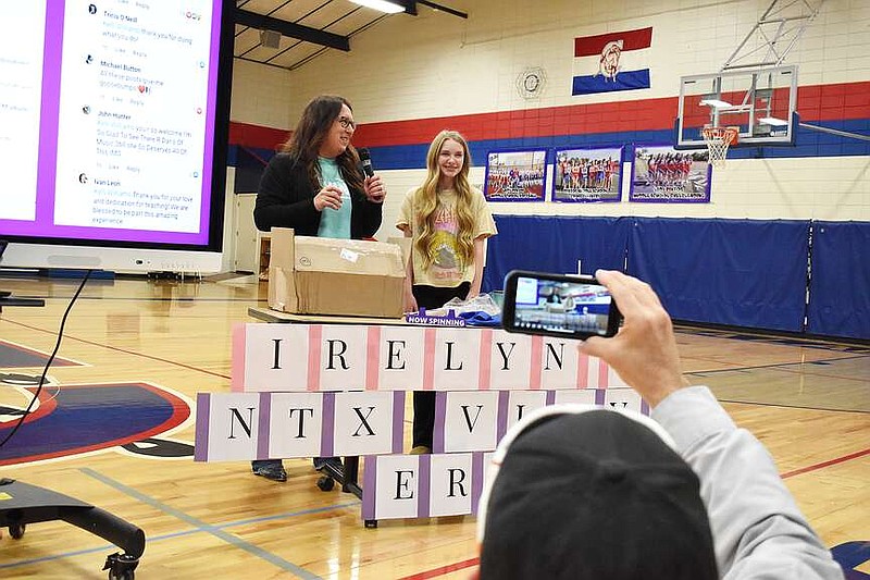 Democrat photo/Garrett Fuller — Irelyn Moseley, right, smiles as she opens gifts Friday with the help of her teacher, Kelli Williams, left, during a surprise assembly in the California Middle School gymnasium. Moseley wrote to North Texas Vinyl, a small, family-owned record store chain in the Dallas-Fort Worth area, for an optional assignment about entrepreneurship in Williams' 7th grade reading class. North Texas Vinyl's owner, G.I. Sanders, responded by sending Moseley a turntable, speakers and records. After he posted her letter on the record store's Now Spinning Facebook Group, hundreds of people from around the world raised $1,500 for a listening initiative at the school, which was matched by Moseley's parents. Sanders said many watched Moseley's reaction unfold in real time as she unwrapped the gifts, as her father, in the foreground, livestreamed the assembly on the Facebook Group.