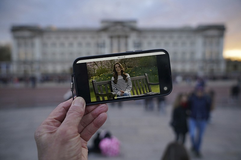 A person watches an announcement on a smart phone outside Buckingham Palace by the Princess of Wales, Friday, March 22, 2024. Kate, the Princess of Wales, says she has cancer and is undergoing chemotherapy. The video announcement Friday came after weeks of speculation spread on social media about her whereabouts and health since she was hospitalized in January for unspecified abdominal surgery. (Yui Mok/PA via AP)