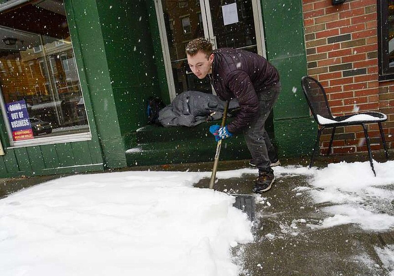 Mikey Reynolds, an employee at The Works on Main Street in Brattleboro, Vt., shovels the sidewalk in front of the restaurant as a person who is facing homelessness sleeps in a door entryway while seeking refuge from the snow storm on Saturday, March 23, 2024. New England is battling a mix of wind, rain, sleet and heavy snow across the region Saturday with more than a foot of snow expected in ski county, but mostly rain, wind and possible flooding in southern areas and along the coast.  (Kristopher Radder  /The Brattleboro Reformer via AP)