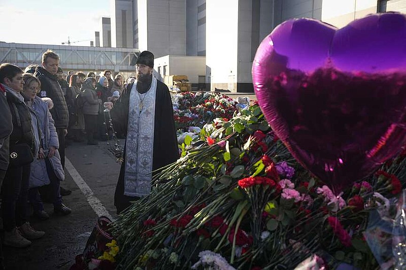 An Orthodox priest conducts a service at a makeshift memorial in front of the Crocus City Hall in the outskirts of Moscow, Russia, Monday, March 25, 2024. There were calls Monday for harsh punishment for those behind the attack on the Rossiya concert hall that killed more than 130 people as authorities combed the burnt-out ruins of the shopping and entertainment complex in search of more bodies. (AP Photo/Alexander Zemlyanichenko)