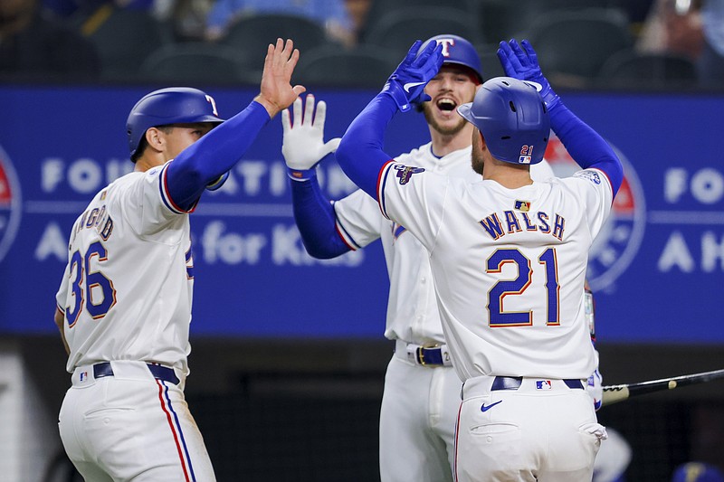 Texas Rangers' Wyatt Langford (36), Jared Walsh (21), and Jonah Heim, back, celebrate Walsh's two-run home run during the second inning of the team's baseball game against the Chicago Cubs, Saturday, March 30, 2024 in Arlington, Texas. (AP Photo/Gareth Patterson)
