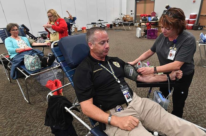 Fayetteville Police Chief Mike Reynolds (center) gives blood Wednesday, April 13, 2022, with help from Vicki Pearson, a donor specialist with Community Blood Center of the Ozarks, during a blood drive at the Fayetteville Town Center. The drive was held on April 13 in honor of the late Fayetteville Police Officer Stephen Carr. Carr, who was killed in 2019 in the line of duty and held Badge No. 413. Visit nwaonline.com/220414Daily/ for today's photo gallery. 
(NWA Democrat-Gazette/Andy Shupe)