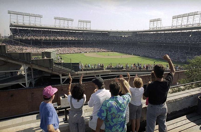 FILE - In this Monday, July 9, 1990, file photo, spectators watch an All-Star Game practice session from the roof of a building just outside Chicago's Wrigley Field.  Booking hotels for baseball games during shoulder seasons like May, June or September can often be cheaper than the summer months. Additionally, save money by planning to attend weekday versus weekend games. (AP Photo/Seth Perlman, File)