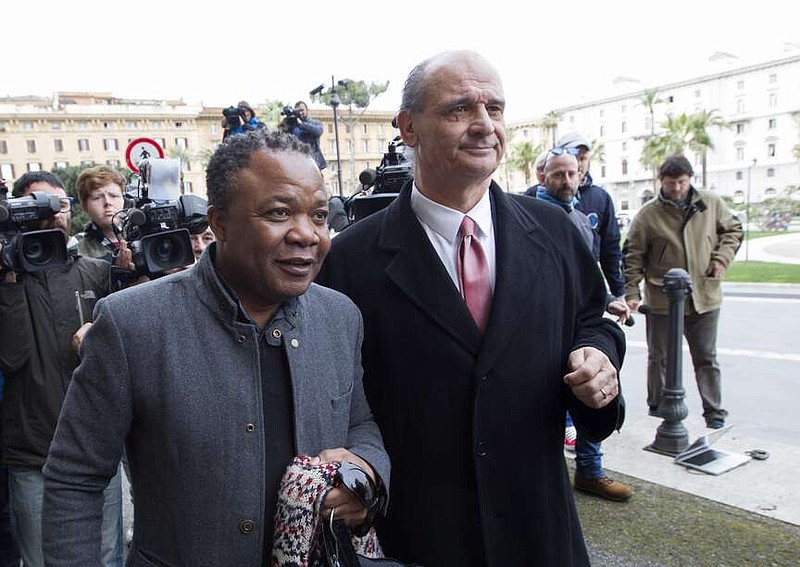 FILE- Diya "Patrick" Lumumba, left, a Congolese citizen who was originally jailed for the murder of Meredith Kercher, flanked by his lawyer Carlo Pacelli, arrives at the Italy's highest court building, in Rome, Friday, March 27, 2015. Amanda Knox faces yet another trial for slander against Lumumba in a case that could remove the last remaining guilty verdict against her nine years after Italy's highest court definitively threw out her conviction for the murder of her 21-year-old British roommate, Meredith Kercher. (AP Photo/Riccardo De Luca, File)