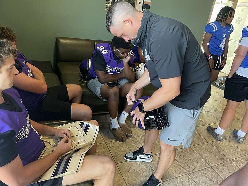 Fayetteville Coach Casey Dick helps one of his players with putting decals on his helmet before the Bulldogs' photo session Thursday morning during the Northwest Arkansas Democrat-Gazette media day at Arvest Ballpark in Springdale. (Henry Apple photo)