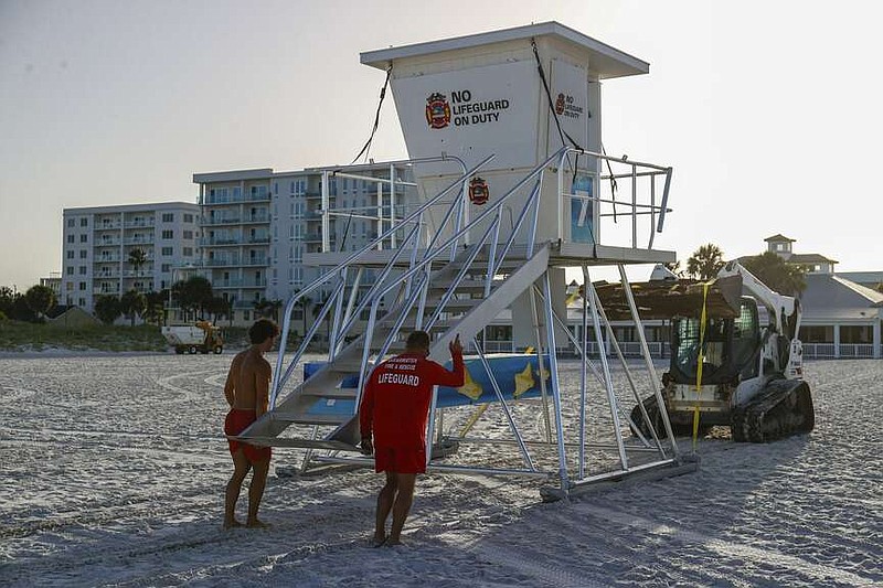 From left, Matthew Blowers and Patrick Brafford prepare to secure a lifeguard tower in preparation of potential storm at Clearwater Beach on Saturday, Aug. 3, 2024, in Clearwater, Fla.  (Jefferee Woo/Tampa Bay Times via AP)