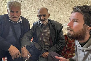 In this photo provided by the Syrian Emergency Task Force, American Travis Timmerman, right, sits with Mosaed al-Rifai, center, who found him in the Syrian desert, and the owner of the house where he took refuge, left, name not available, in Damascus, Syria on Thursday Dec. 12, 2024. (Syrian Emergency Task Force via AP)