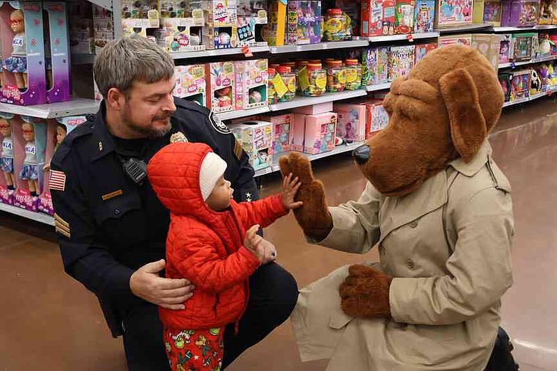 Pine Bluff police Sgt. Christopher Wieland helps a child high-five McGruff the Crime Dog at the Pine Bluff Fraternal Order of Police's Fourth Annual Shop with a Cop event, held Friday Dec. 12, 2025, at the Pine Bluff Walmart Supercenter. (Special to The Commercial/Pine Bluff Police Department)