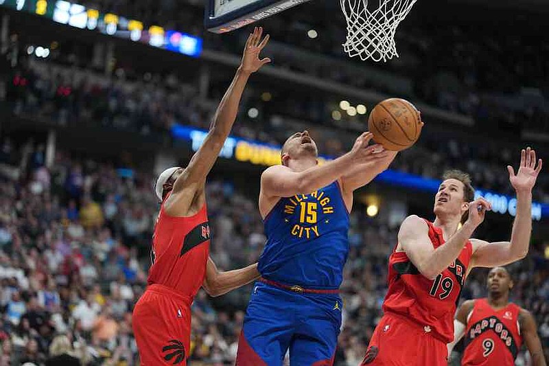 El pívot de los Denver Nuggets, Nikola Jokic, conduce hacia la canasta entre el delantero de los Toronto Raptors, Brandon Ingram, izquierda, y el centro Jakob Poeltl, derecha, en la primera mitad de un partido de baloncesto de la NBA el viernes 20 de marzo de 2026 en Denver. (Foto AP/David Zalubowski)