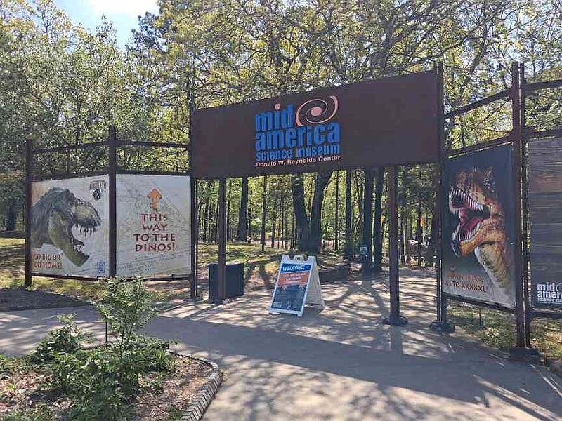 The entrance gate to Mid-America Science Museum features signs for an upcoming dinosaur exhibit. (The Sentinel-Record/Will Livingston)