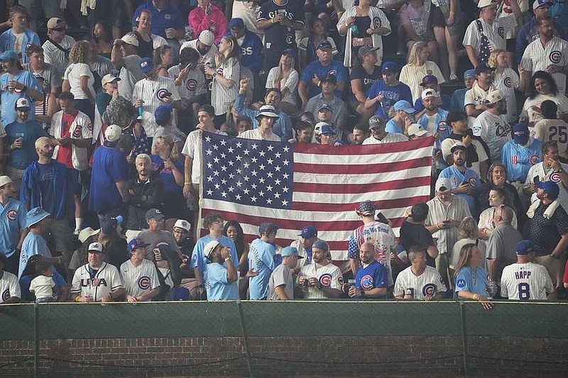 Los fanáticos sostienen una bandera de los Estados Unidos en las gradas durante la sexta entrada de un juego de béisbol entre los Cachorros de Chicago y los Cardenales de San Luis, el sábado 4 de julio de 2026, en Chicago. (Foto AP/David Banks)