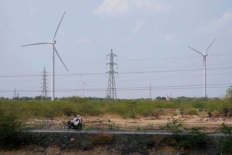 FILE - A motorcyclist ride past wind turbines, an Adani Group project, near Sadla village in Surendranagar district of Gujarat state, India, March 20, 2023. (AP Photo/Ajit Solanki, File)
