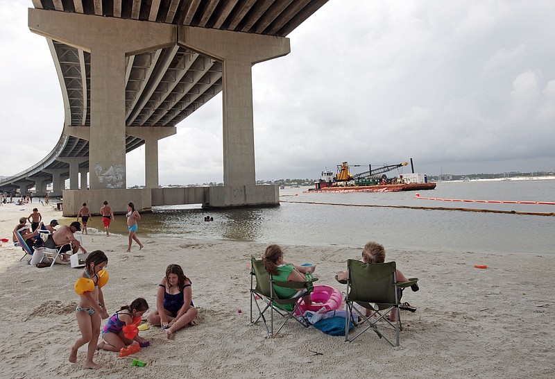 Sunbathers watch booming operations in the Perdido Pass as they sit in the shade under the Perdido Pass bridge in Orange Beach, Ala., Sunday, June 6, 2010. Alabama booming operations are being ramped up with oil  from the Deepwater Horizon disaster approaching the coast. (AP Photo/Dave Martin)