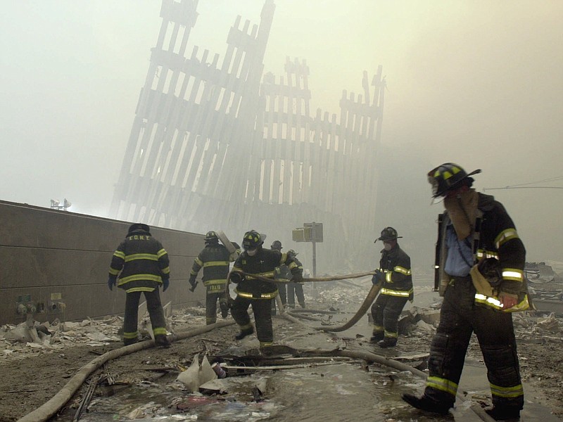 In this Tuesday, Sept. 11, 2001 file photo, with the skeleton of the World Trade Center twin towers in the background, New York City firefighters work amid debris on Cortlandt St. after the terrorist attacks. (AP Photo/Mark Lennihan)