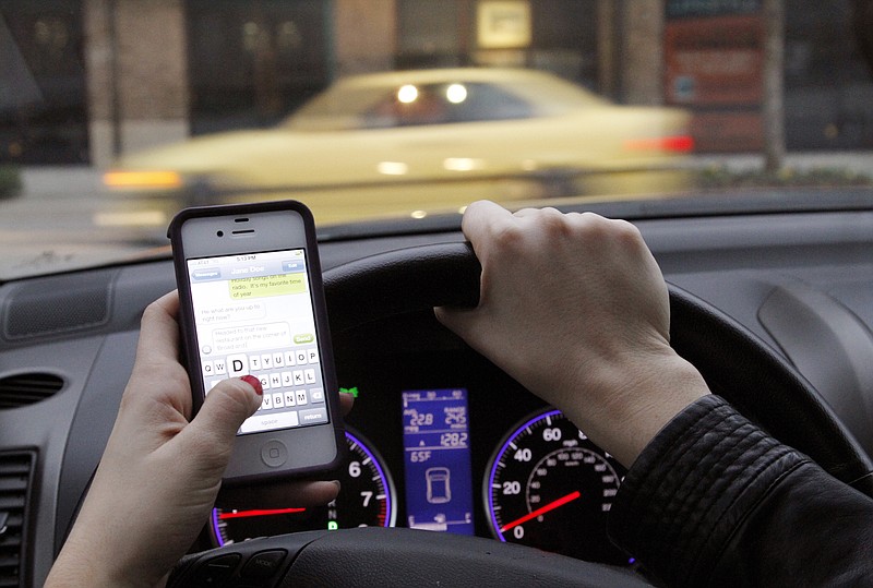 A Chattanooga motorist holds an iPhone 4S while driving on Thursday. The National Transportation Safety Board declared last week that texting, emailing or chatting on a cellphone while driving is too dangerous to be allowed and urged all states to ban any cellphone use behind the wheel except for emergencies.