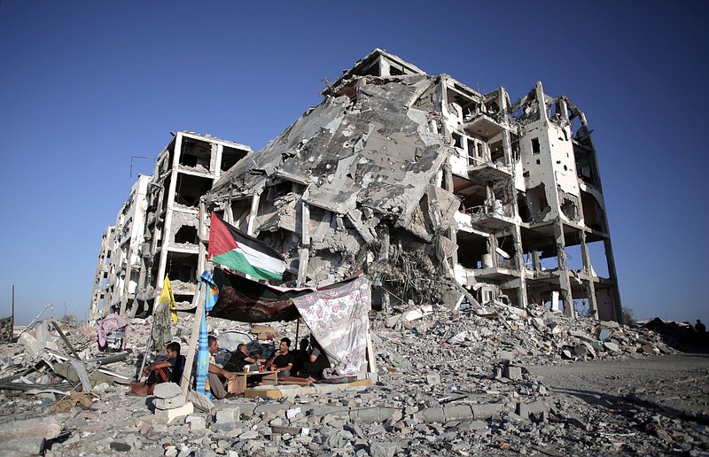 
              FILE- In this Monday, Aug. 11, 2014 file photo, Palestinian Ziad Rizk, sits with others in a shelter made of a blanket stretched over four poles next to one of the destroyed al-Nada Towers, where he lost his apartment and clothes shop, in the town of Beit Lahiya, northern Gaza Strip. Dozens of residents the al-Nada Towers took advantage of the latest truce to visit their homes, salvage what they can and exchange tips on how best to seek and secure compensation for their homes. (AP Photo/Khalil Hamra, File)
            