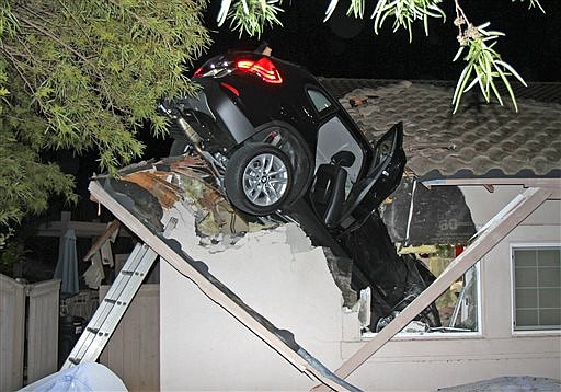 This photo provided by homeowner George Strother shows a sport utility vehicle that went airborne and sailed into the roof of his home in Escondido, Calif., around 12:30 a.m. Wednesday, Dec. 10, 2014. Police said a BMW driver lost control during a turn, went off a road and plunged through the garage roof of a home that sits about 20 feet below the roadway. Strother said the car landed on the hood of his Nissan Pathfinder in the garage and knocked the ceiling down on another car. Neither he nor his wife, or the driver of the car, were hurt.