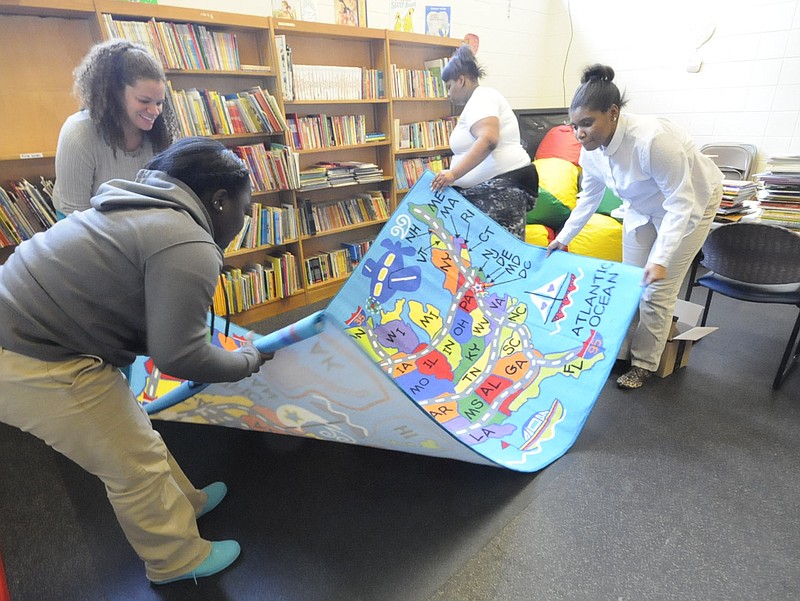 Alonna Gardner, left, and Leonia Barber place a new rug on the floor of the Brainerd Recreation Center's reading room Wednesday as part of their On Point volunteer work for United Way while Elizabeth Tallman, top left, director of graduation initiatives for United Way, watches. Five students from Brainerd High School volunteer each week at the center to help younger students stay on track for graduation.