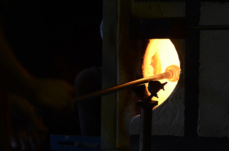 Matt Thomas pulls a glass Christmas tree ornament out of a furnace at the Ignis Glass Gallery on Broad Street on Wednesday.