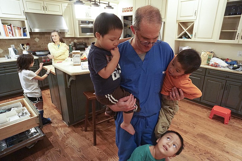 Sarah Risley speaks with her daughter Laura Ann at left  as her husband Dr. Jon Risley interacts with his adopted sons Nehemiah, Gabriel and Seth, from left, after arriving home from work. The Risley family have felt a religious calling to go to China and adopt three more children this December which will bring the total number of kids they support to 13. 