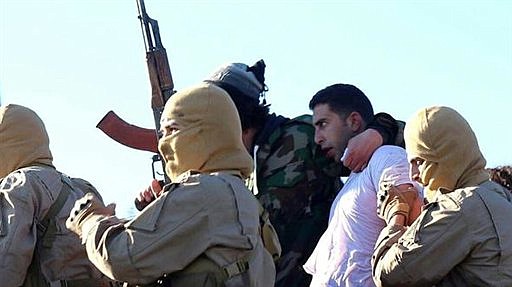 This image posted by the Raqqa Media Center, which monitors events in territory controlled by Islamic State militants with the permission of the extremist group, shows militants with a captured pilot, center right, wearing a white shirt in Raqqa, Syria, on Dec. 24, 2014. 