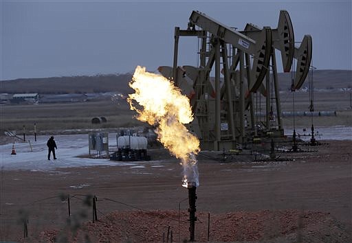 Workers tend to oil pump jacks behind a natural gas flare near Watford City, N.D., in this Dec. 17, 2014.