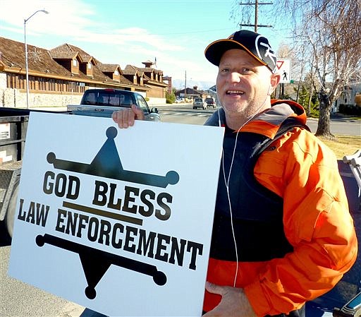 In this Dec. 22, 2014, photo, passing motorists honk as retired Douglas County sheriff's deputy John Munk of Gardnerville, Nev., holds a sign showing his support for law enforcement, in front of the Minden Post Office south of Carson City.