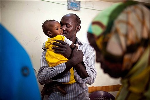 In this Oct. 4, 2014, photo released by the International Organization for Migration, 33-year-old Ibrahim Hassan, from Tununu, a village in North Darfur, Sudan, holds a child, as he waits to use a pay phone to call his family, in Cairo, Egypt. 