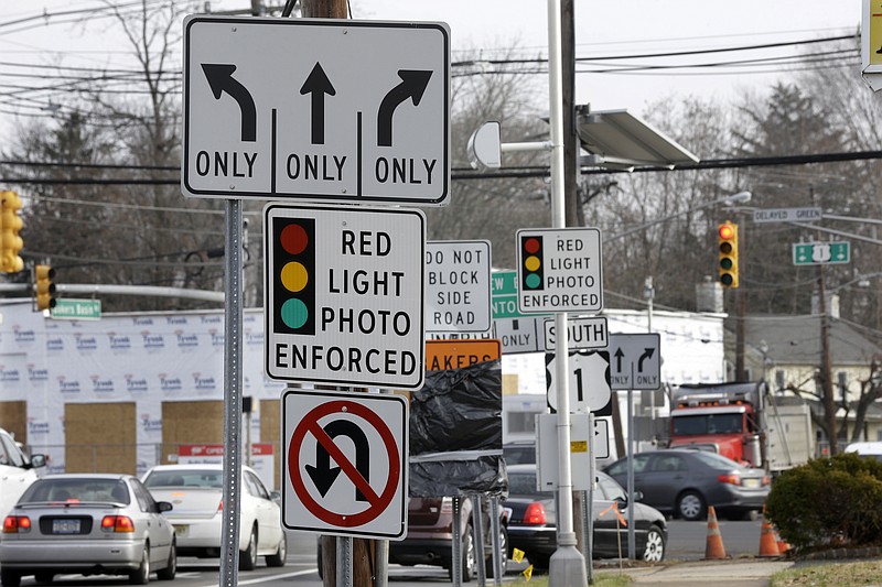 In a Tuesday, Dec. 16, 2014, file photo, traffic passes a red light photo enforcement sign below a red light camera at the intersection of Route 1 and Franklin Corner Road, in Lawrence Township, N.J. 