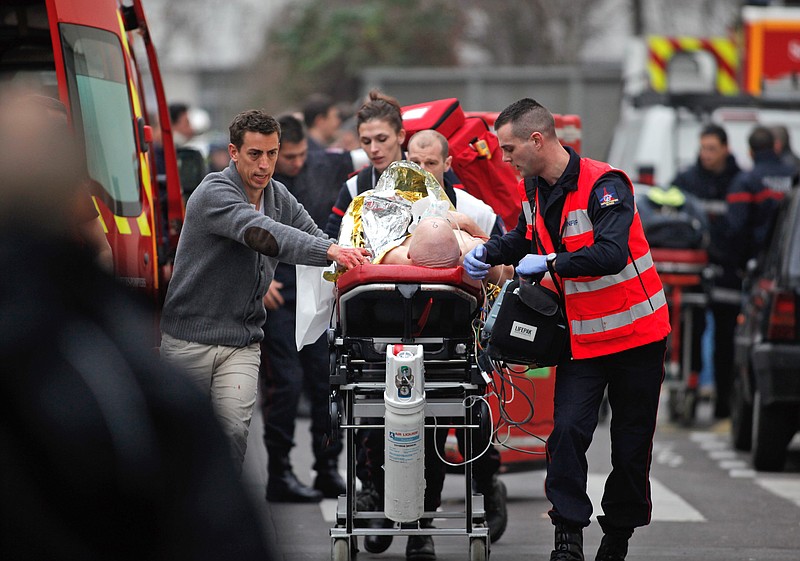 An injured person is transported to an ambulance after a shooting, at the French satirical newspaper Charlie Hebdo's office, in Paris, Wednesday, Jan. 7, 2015. Masked gunmen stormed the offices of a French satirical newspaper Wednesday, killing at least 11 people before escaping, police and a witness said. The weekly has previously drawn condemnation from Muslims. 