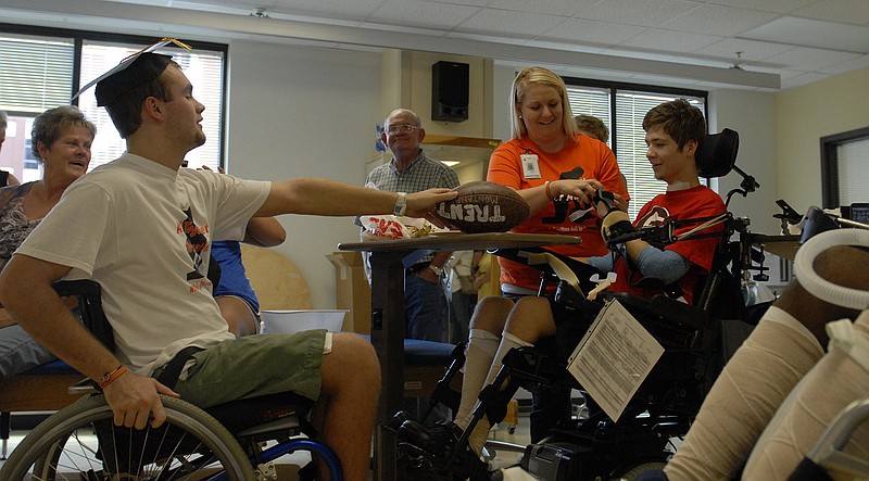 In this file photograph from 2012, then-15-year-old Austin Whitten passes a signed football to a fellow patient after Whitten's graduation from the inpatient program at the Shepherd Center in Atlanta, a hospital specializing in rehabilitation for people with spinal and brain injuries. The former football, basketball and baseball player from LaFayette, Ga., broke his neck after jumping into a pond, an injury that left him paralyzed.