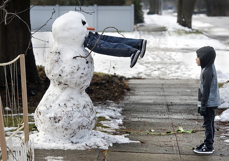 Miles McQuesten, 5, stands in front of a snowman in Spokane, Wash. The boy and his father, Rick, built the snowman Friday morning, creating legs constructed from branches and newspapers. 