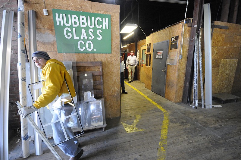 Glass cutter Anthony Wilson, left, moves a piece to the cutting table at Hubbuch Glass as President Don Johnson, back center, and Senior Vice President Bob Cummins approach the work area following the yellow line.