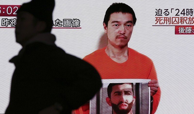 A man walks by a screen showing TV news reports of a YouTube posted by a militant group on Jan. 27, purportedly showing a still photo of Japanese hostage Kenji Goto holding what appears to be a photo of Jordanian pilot Lt. Muath al-Kaseasbeh, in Tokyo, in this Jan. 28, 2015 photo.