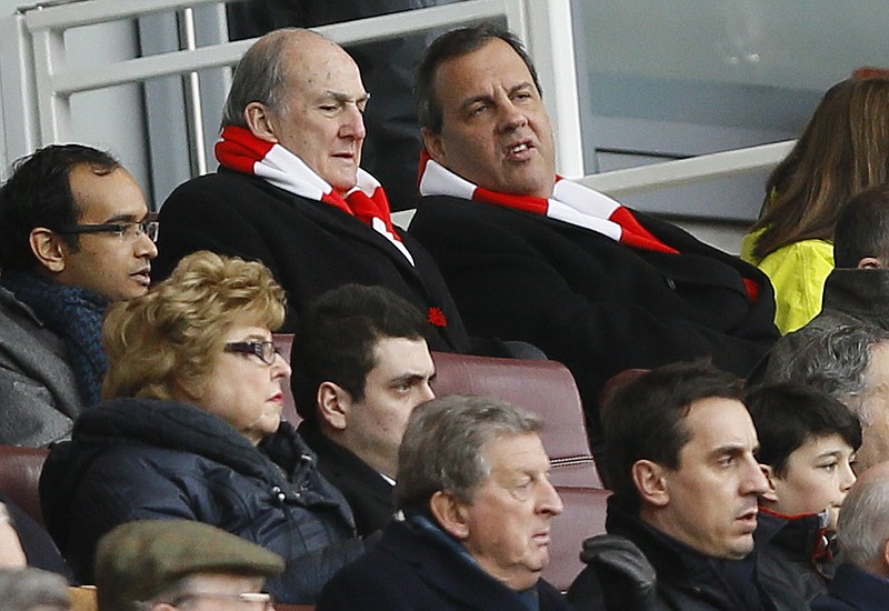 
              New Jersey Gov. Chris Christie, top right, wearing an Arsenal scarf, sits with Rutgers University President Robert Barchi, left, in the stands during the English Premier League soccer match between Arsenal and Aston Villa at the Emirates stadium in London, Sunday, Feb. 1, 2015.  Pictured at bottom center is England international coach Roy Hodgson, with former England international player Gary Neville, bottom right. (AP Photo/Kirsty Wigglesworth)
            