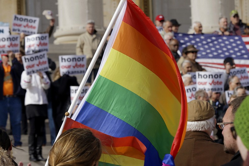 
              FILE -  In this Nov. 19, 2014, file photo, supporters of Arkansas' law banning same sex marriage, top, hold a rally as a protestor waves a rainbow flag at the Arkansas state Capitol in Little Rock, Ark. Americans are slightly more likely to favor than oppose allowing gay and lesbian couples to legally marry, a new Associated Press-GfK poll finds, but most believe wedding-related businesses should be allowed to deny service to same-sex couples for religious reasons. (AP Photo/Danny Johnston, File)
            