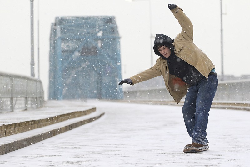 Cory Mansel, 23, uses a skateboard deck as a makeshift snowboard to skid across the Walnut Street bridge as snow falls in Chattanooga on Wednesday, February 18, 2015.