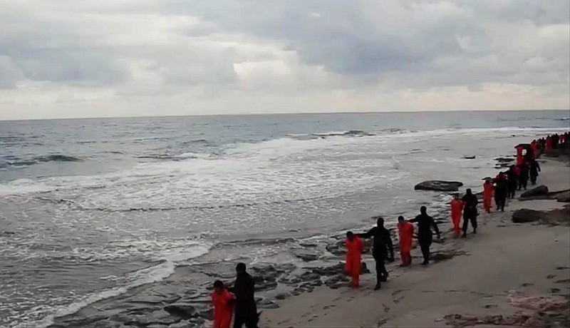 In this file image made from a video released Sunday, Feb. 15, 2015 by militants in Libya claiming loyalty to the Islamic State group purportedly shows Egyptian Coptic Christians in orange jumpsuits being led along a beach, each accompanied by a masked militant. 