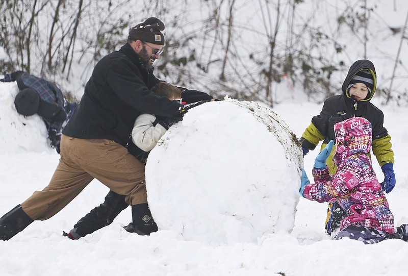 William Meager and his son Benjamin Meager, left, work with Scotty Purdue and his sister Sara Purdue to roll a huge snowball while at Red Bank's White Oak park on Thursday morning, February 26, 2015. An overnight winter storm dumped over half of a foot of snow on the Tennessee Valley area. 
