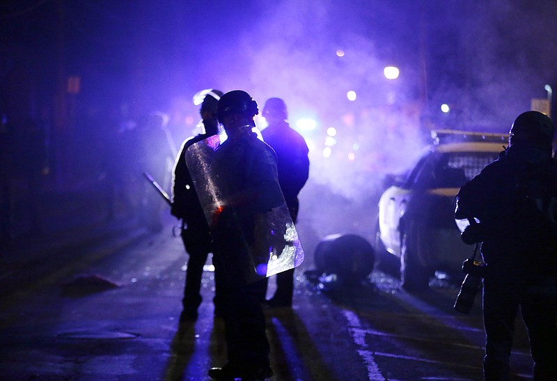 In this Nov. 25, 2014, file photo, police officers watch protesters as smoke fills the streets in Ferguson, Mo. after a grand jury's decision in the fatal shooting of Michael Brown.