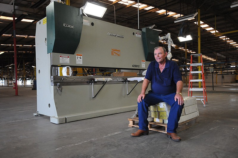 Randy Phillips, owner and president of Phillips Bros. Machine Co., sits next to his first new piece of equipment, a 14-ton press designed to shape steel, inside his company's new location at the former Bluebird manufacturing plant in LaFayette in 2012.