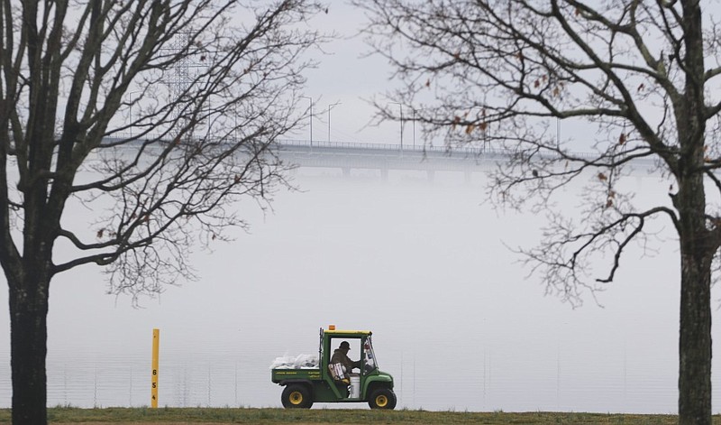 Larry Redden, a maintenance worker with TVA, picks up trash along the shoreline of Chickamauga Lake as fog obscures the dam early Tuesday morning. 