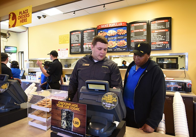 General Manager Dylan Thompson, left, and Victor Mitchell talk at the register of the newly remodeled Zaxby's on Shallowford Road.