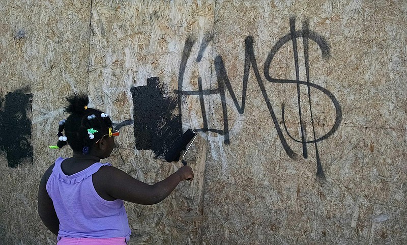 Kadesha Cook, 8, works with police to paint over graffiti on a building near Glass Street on Monday afternoon.