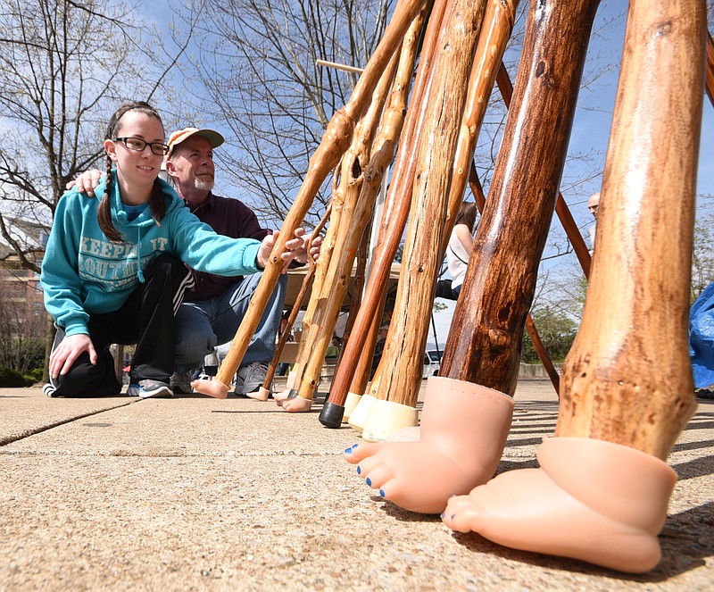 Courtney Moore, left, replaces a walking stick to its position Saturday at the Chattanooga River Market. "Mr. Twisted" is the creation of David Moore, second from left, a display of homemade walking sticks with doll feet attached as a base. The annual event was held on the Tennessee Aquarium Plaza in downtown Chattanooga.