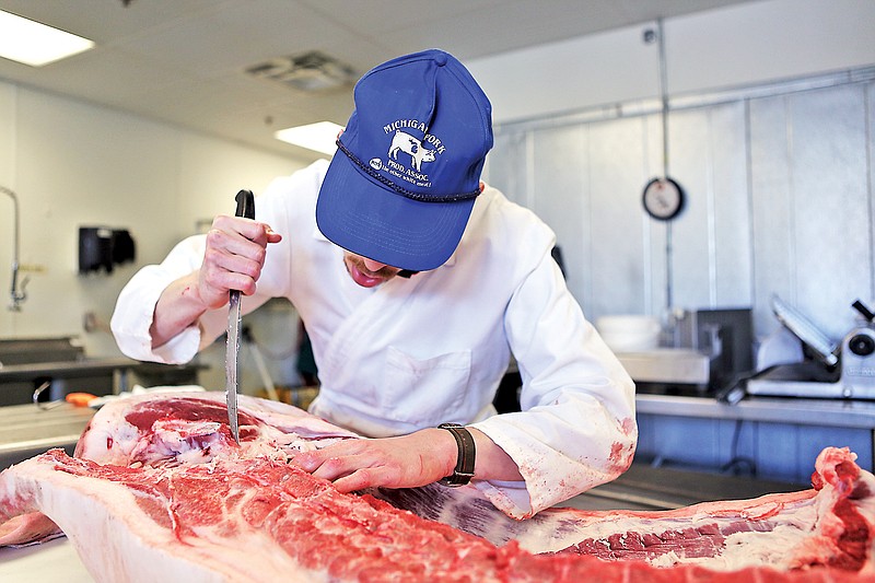 Milton White, a butcher at Main Street Meats, slices into a halved hog at the shop. Main Street Meats butchers whole animals on site and typically gets in three pigs a week.