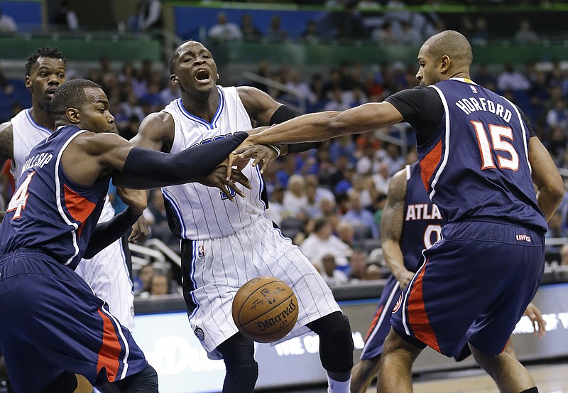 Orlando Magic's Victor Oladipo, center, loses the ball as he is fouled by Atlanta Hawks' Al Horford (15) as Hawks' Paul Millsap (4) defends during their game, Wednesday, March 25, 2015, in Orlando, Fla. 