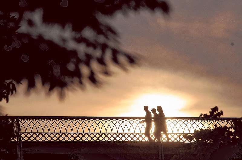 Three people walk together across the Walnut Street Bridge as the sun sets.